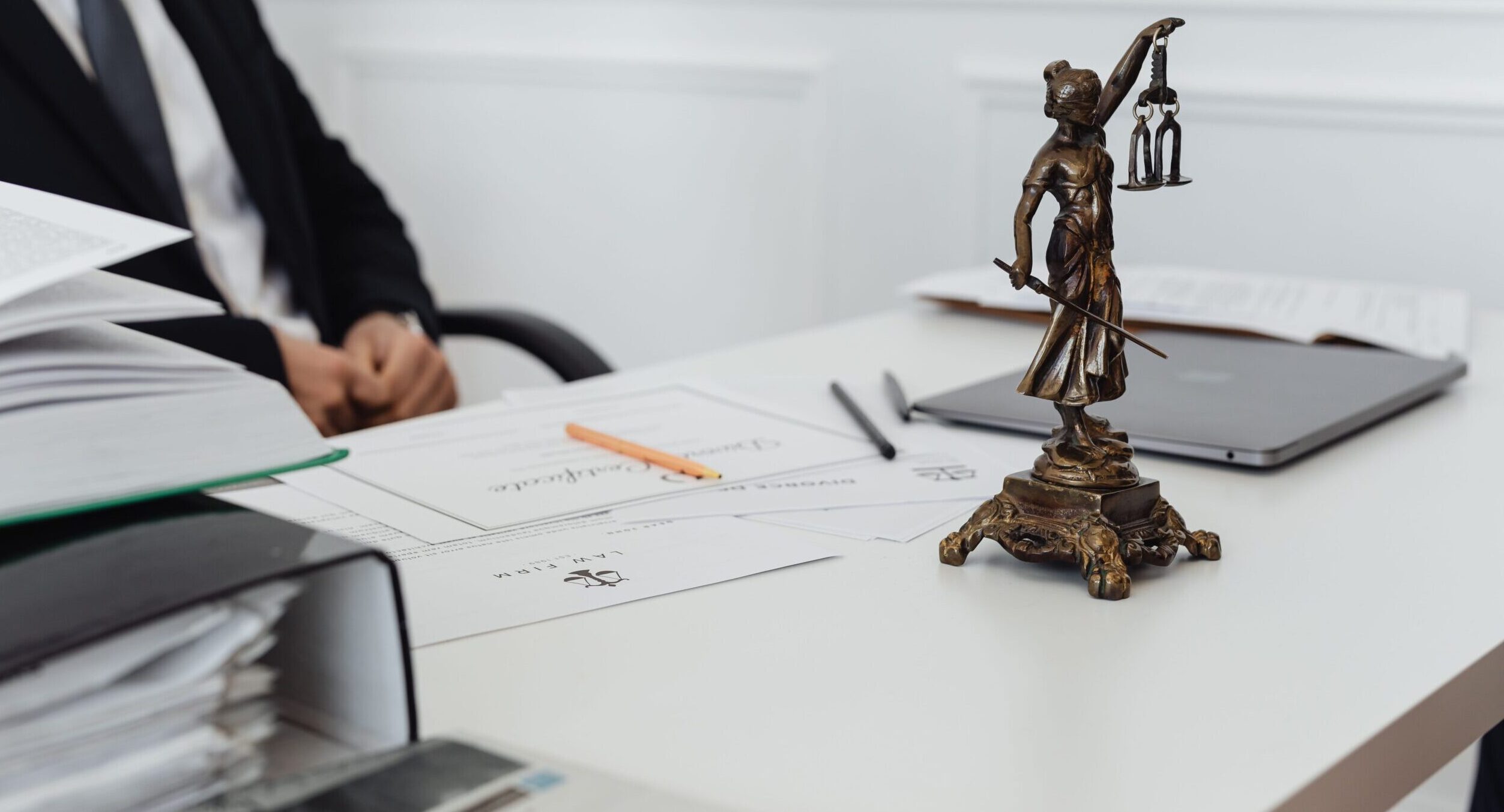 A legal professional's workspace featuring Lady Justice statue, documents, and a laptop.